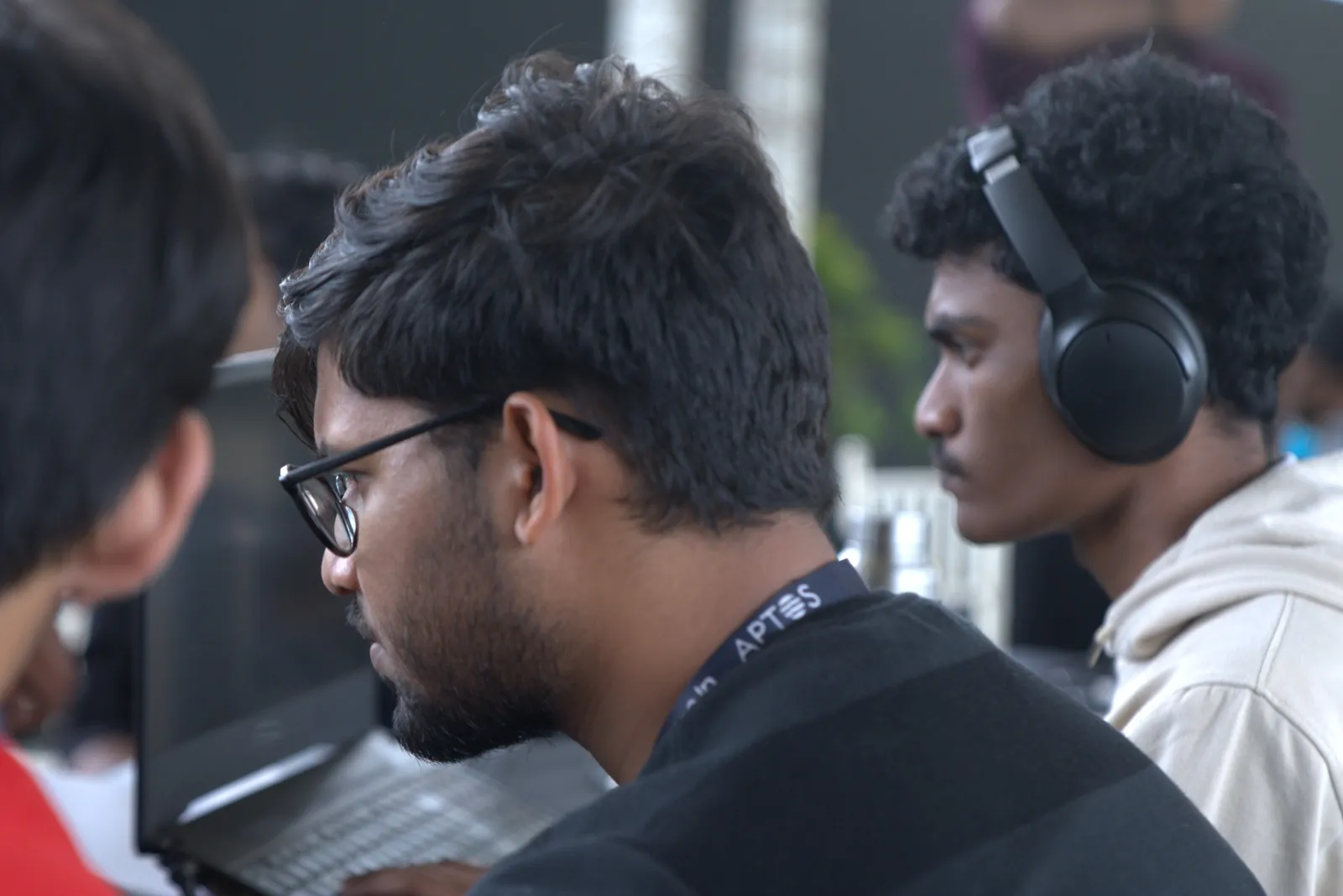 Ujesh at his laptop, a teammate in headphones beside him